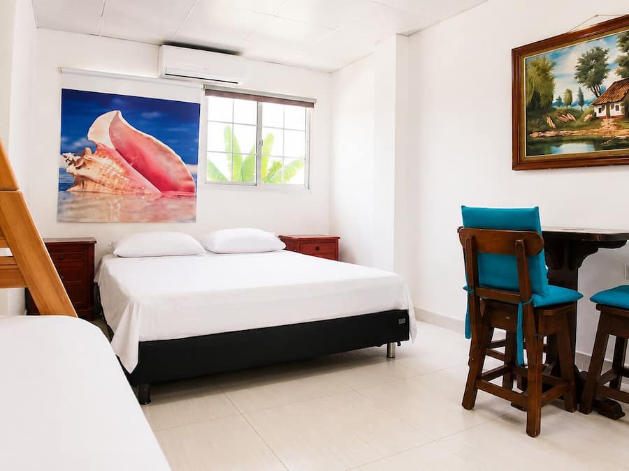 Un dormitorio con una cama, un escritorio con dos sillas, una ventana y un cuadro en la pared.
