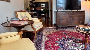 A living room with a television, a sofa, a coffee table, a patterned rug, and a wooden cabinet. - Suite A at The Elliott 1887 (LeRoy)