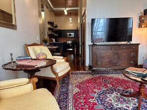A living room with a television, a sofa, a coffee table, a patterned rug, and a wooden cabinet. - Suite A at The Elliott 1887 (LeRoy)