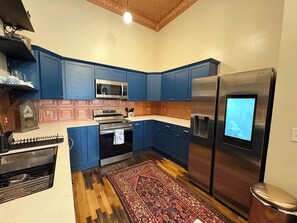 A kitchen with blue cabinets, a stainless steel refrigerator, a microwave, and a stove. - Suite A at The Elliott 1887 (LeRoy)