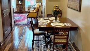 A dining area with a wooden table set for four, a stone wall, and a view of a brick building through a window. - Suite A at The Elliott 1887 (LeRoy)