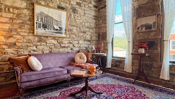 Una habitación con pared de piedra, un sofá morado, un tapete estampado y un cuadro enmarcado.