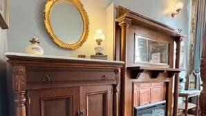A room with a wooden cabinet, a mirror with a gold frame, a fireplace, and a patterned rug. - Suite A at The Elliott 1887 (LeRoy)