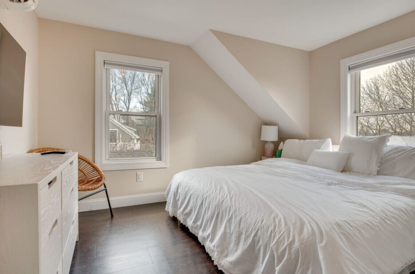 Un dormitorio con cama, escritorio, silla y dos ventanas.