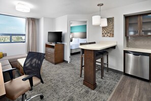 Une chambre d’hôtel équipée d’un lit, d’un bureau, d’une chaise, d’une télévision et d’une kitchenette, avec vue sur la ville.