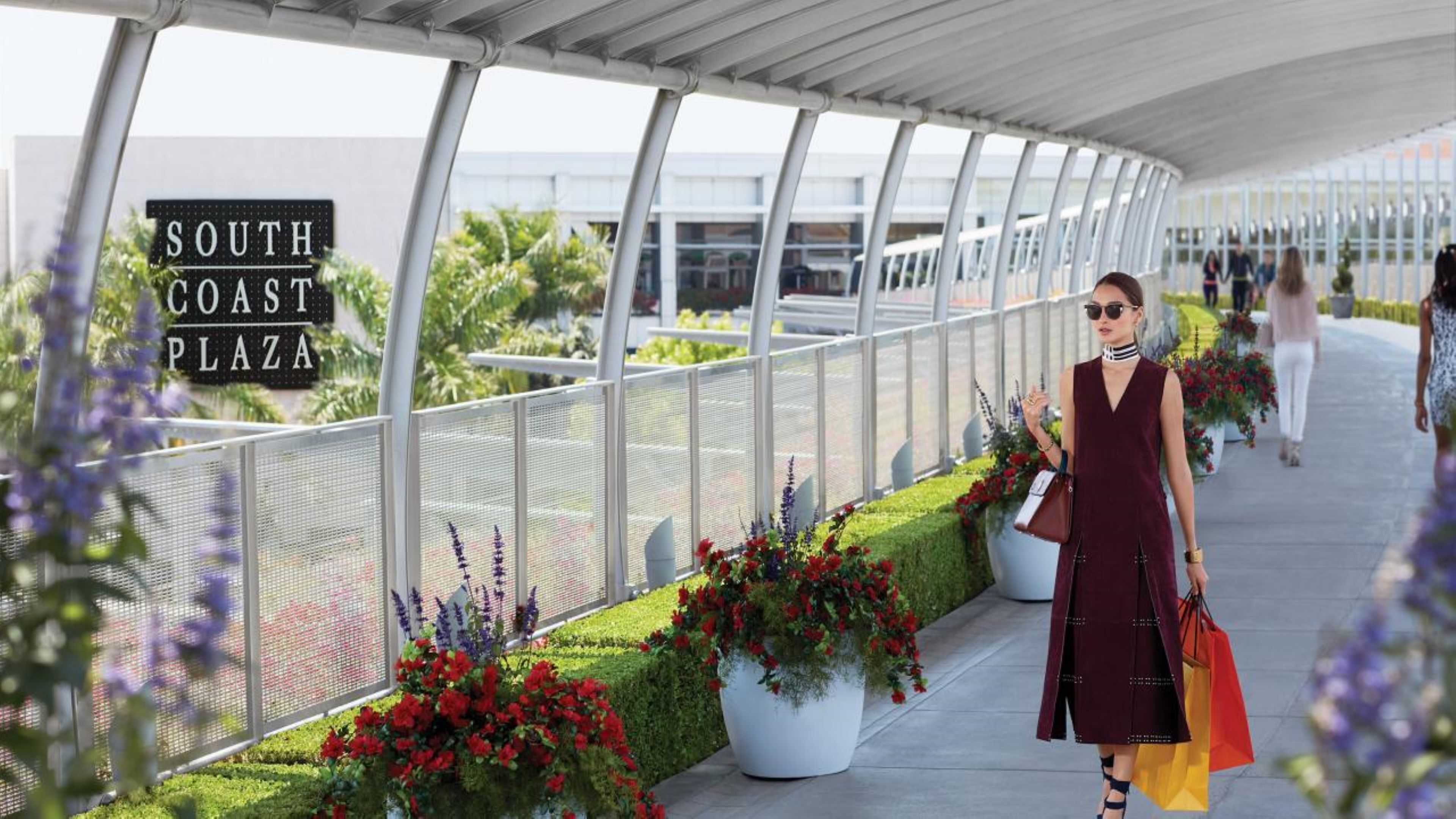 Une allée couverte, agrémentée d’un panneau indiquant « South Coast Plaza », de plantes en pot et de passants.