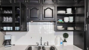A kitchen with dark wooden cabinets, a white tiled backsplash, a double sink, and a coffee maker. - Great Home_ Sleeps 10_Close to Arrowhead_Football (Independence)
