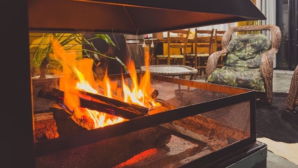 Een metalen vuurkorf met vlammen, omringd door rieten meubels en stoelen.