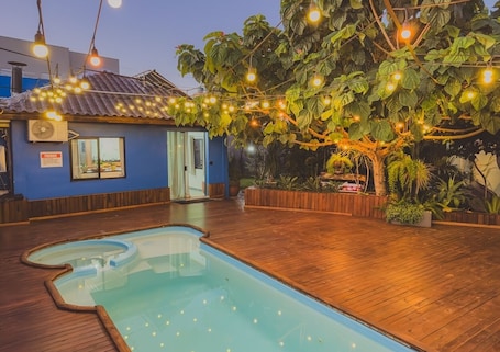 A pool area with a wooden deck, a small building with a blue exterior, and string lights.. Cabana Raízes with Hot Tub, Fireplace and Private Pool.