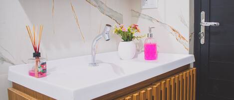 Une salle de bain avec un lavabo blanc, un meuble en bois, un mur en marbre et une porte noire.