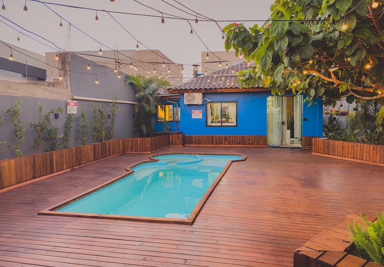 Uma área de piscina no terraço com deck de madeira, um edifício azul e luzes de corda.