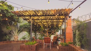Een terras buiten met houten vloer, een pergola met lichtslingers en zithoekjes.