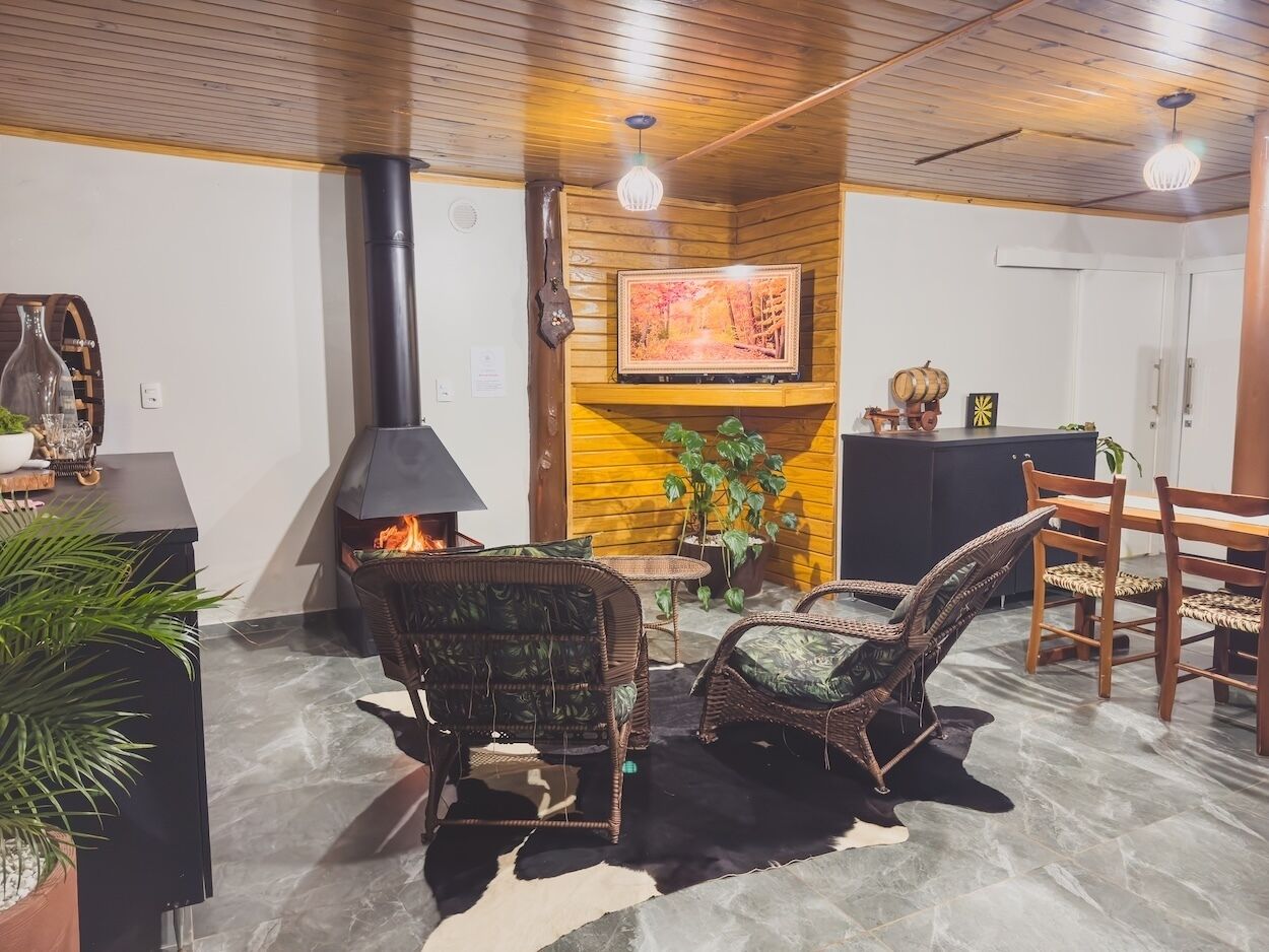 A cozy living room with a fireplace, wicker chairs, a dining table, and a potted plant.
