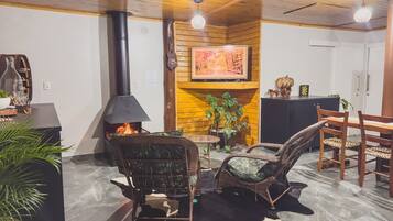 A cozy living room with a fireplace, wicker chairs, a dining table, and a potted plant.
