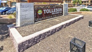 Un cartel da la bienvenida a visitantes en Tolleson, con un logotipo y una vista clara del área de estacionamiento circundante.