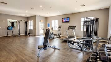 A spacious gym with cardio machines, weight benches, and a television screen.