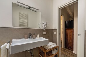 Une salle de bain équipée d’un lavabo, d’un miroir, d’un porte-serviettes et d’un sèche-cheveux fixé au mur.