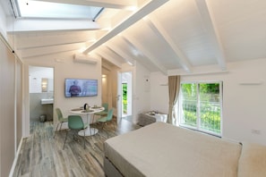 Quarto com cama, mesa de jantar com cadeiras, TV e uma janela grande com vista para o verde.