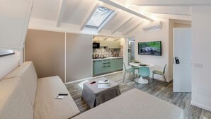 Een modern interieur met een loft-plafond, een kitchenette, een eethoek en een woonruimte met een bank en voetenbankje.