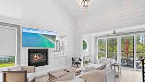 Ein geräumiges Wohnzimmer mit Kamin, bequemen Sitzgelegenheiten, einem Fernseher und großen Fenstern mit Seeblick.