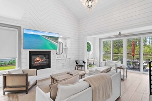Ein geräumiges Wohnzimmer mit Kamin, bequemen Sitzgelegenheiten, einem Fernseher und großen Fenstern mit Seeblick.
