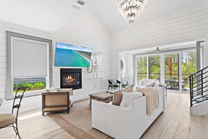 A modern living room with a fireplace, white furniture, a TV, and large windows overlooking a natural landscape. - Walk to the Beach + Close to Seaside | Gated Community | Pond Views - 'Peace of Mind' (Santa Rosa Beach)