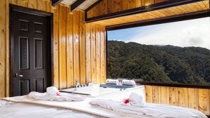 A wooden room with a large window, a black door, and a bed with towels. - Hotel Gema del Bosque (Copey)