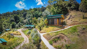 A hillside property with a main building and a smaller structure, surrounded by lush greenery and a winding path. - Hotel Gema del Bosque (Copey)