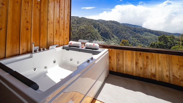 A wooden cabin with a large bathtub and a view of a forested mountain range. - Hotel Gema del Bosque (Copey)