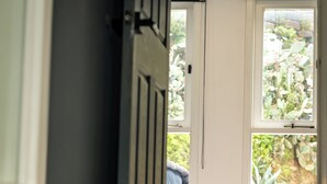 Un pasillo interior con una puerta que da a una habitación con cama y ventana con vistas a un jardín.
