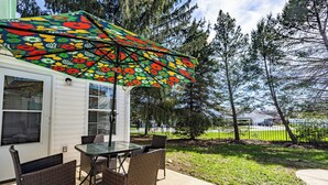 Une terrasse avec une table et des chaises, un parasol, et une vue sur des arbres et une clôture.