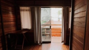 A wooden room with a bench, a sliding door leading outside, and a view of a building through the door. - CABAÑA CASA BLANCA HUACACHINA PERU ACCOMMODATION & TOURS (Huacachina)