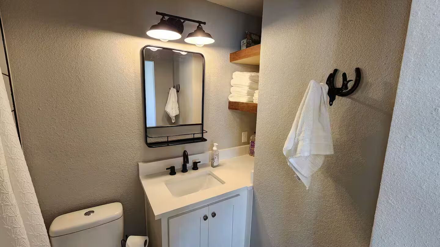 Un baño con un lavamanos blanco, un espejo, un perchero para toallas y un inodoro.