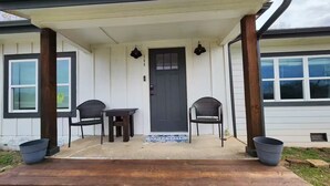 A house with a porch, a door, two chairs, a small table, and a welcome mat. - Spacious Remodeled Home with Huge Backyard (Denison)