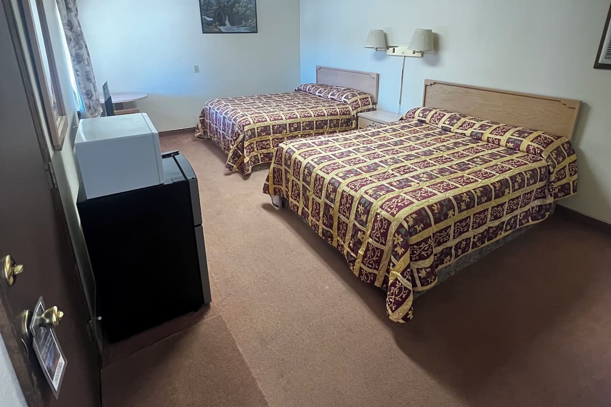 A hotel room with three beds, a desk, a chair, a flat-screen TV, and a ceiling light.