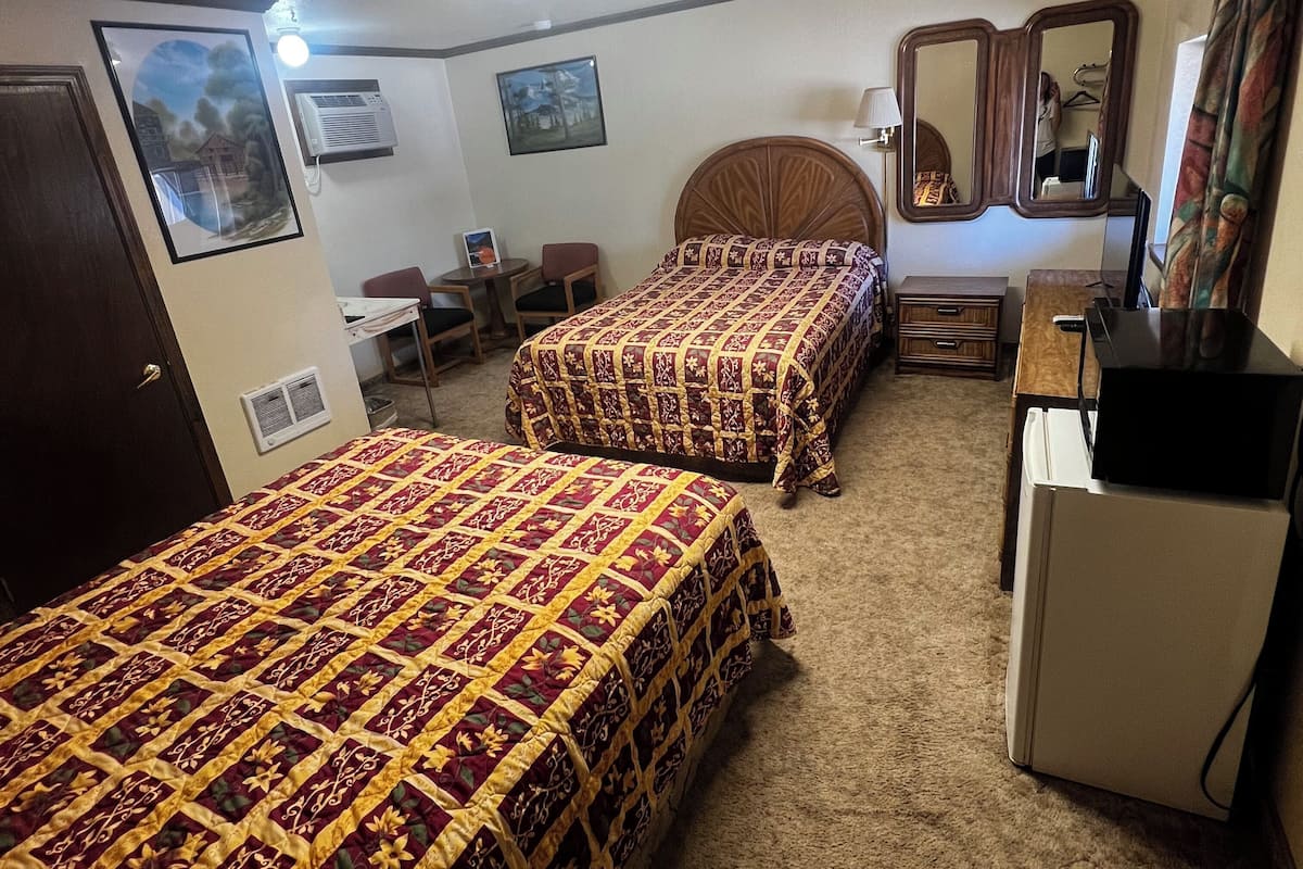 A hotel room with two beds, a desk, a chair, a dresser, a mirror, and a ceiling light.
