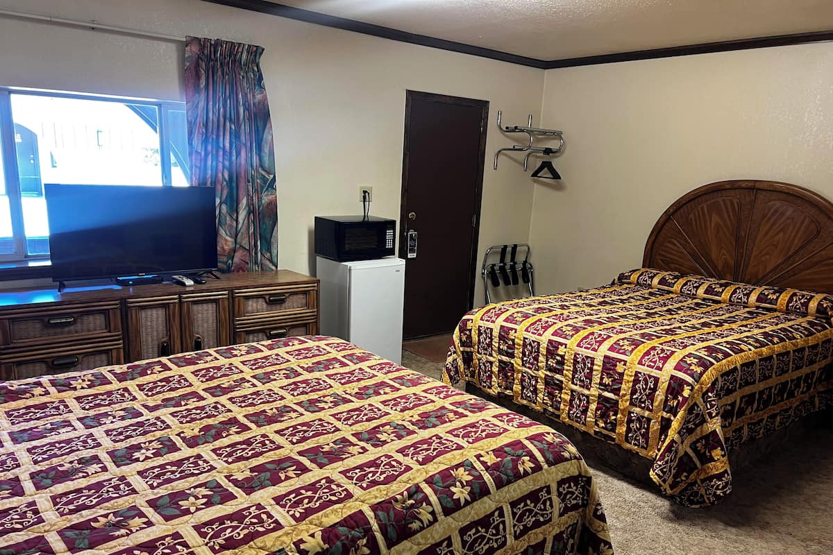 A hotel room with two beds, a television, a refrigerator, and a door with a coat rack.