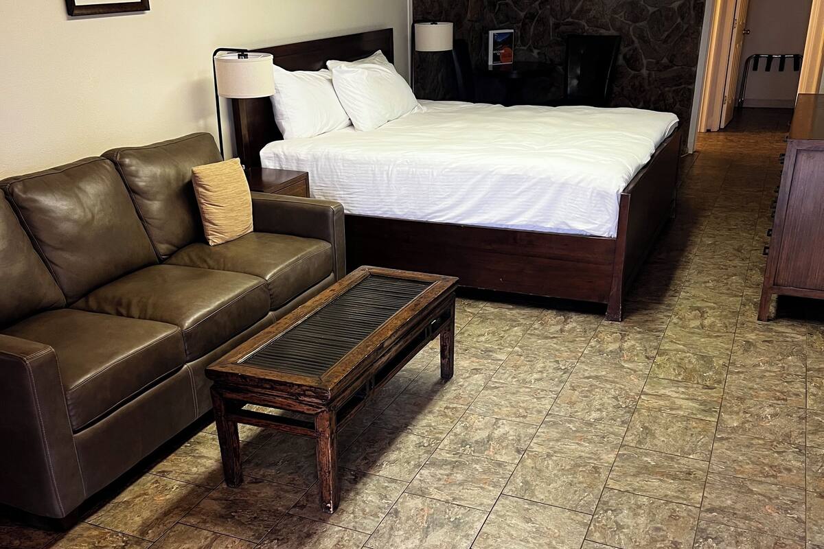 A bedroom with a bed, a leather sofa, a wooden coffee table, and a stone wall.