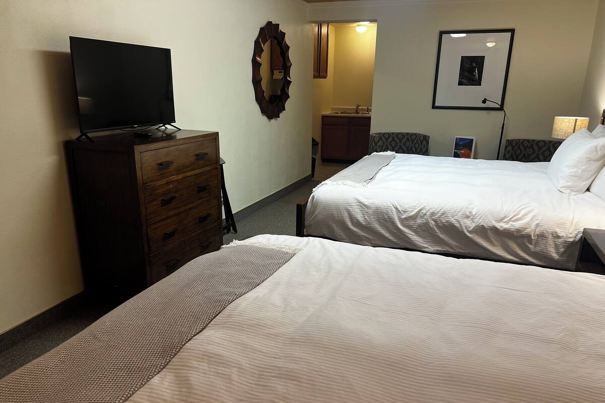 A hotel room with two beds, a television on a dresser, a mirror, and a framed picture on the wall.
