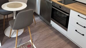 Eine moderne Küche mit weißen Schränken, einem Geschirrspüler, einem Backofen und einem Essbereich mit einem runden Tisch und Stühlen.