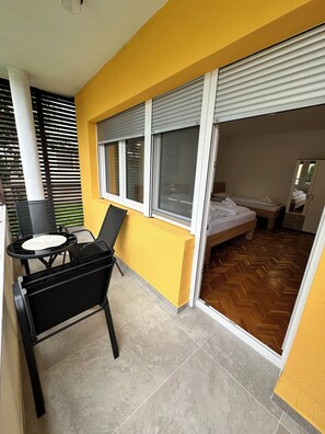 A room with a bed, a small table with chairs, a sliding glass door, and a view of the outside.