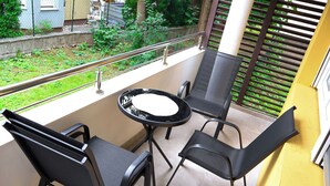 Ein Balkon mit Tisch und zwei Stühlen, einem Geländer und Blick auf Grünflächen.