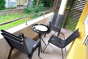 A balcony with a table and two chairs, a railing, and a view of greenery.