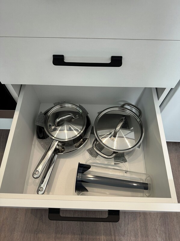 Un tiroir contenant deux casseroles en acier inoxydable et une spatule noire.