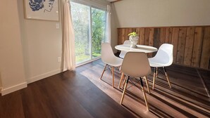 A dining area with a round table, white chairs, a potted plant, and a large window with curtains. - Farmhouse Loft with pond + pasture views in Creal Springs (Creal Springs)