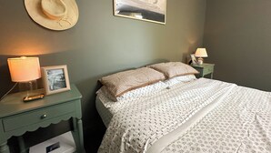 A bedroom with a bed, two nightstands, a lamp, a framed picture, a hat, and a landscape painting on the wall. - Farmhouse Loft with pond + pasture views in Creal Springs (Creal Springs)