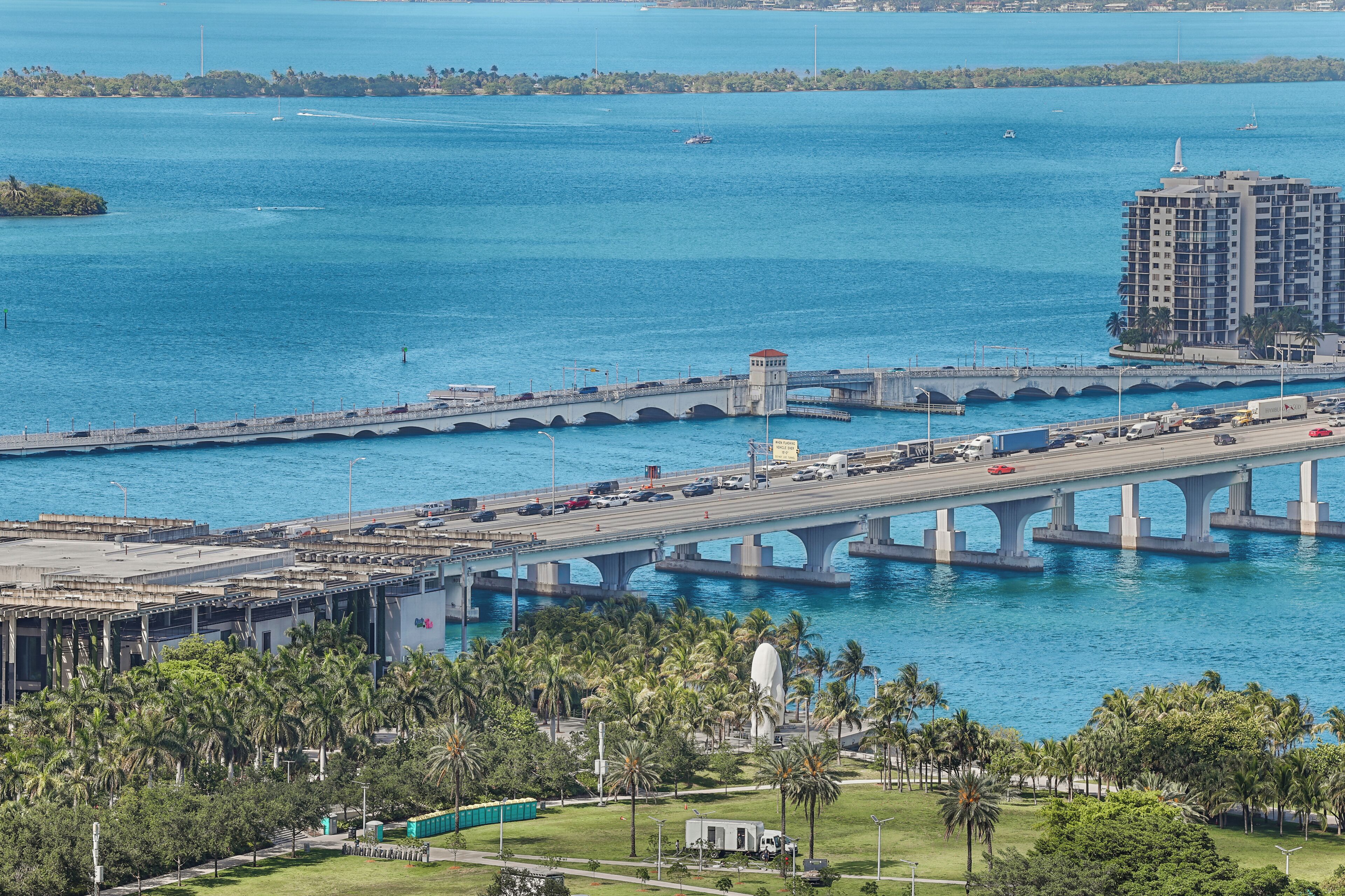 Un pont enjambant une étendue d’eau, avec un bâtiment et des palmiers au premier plan.