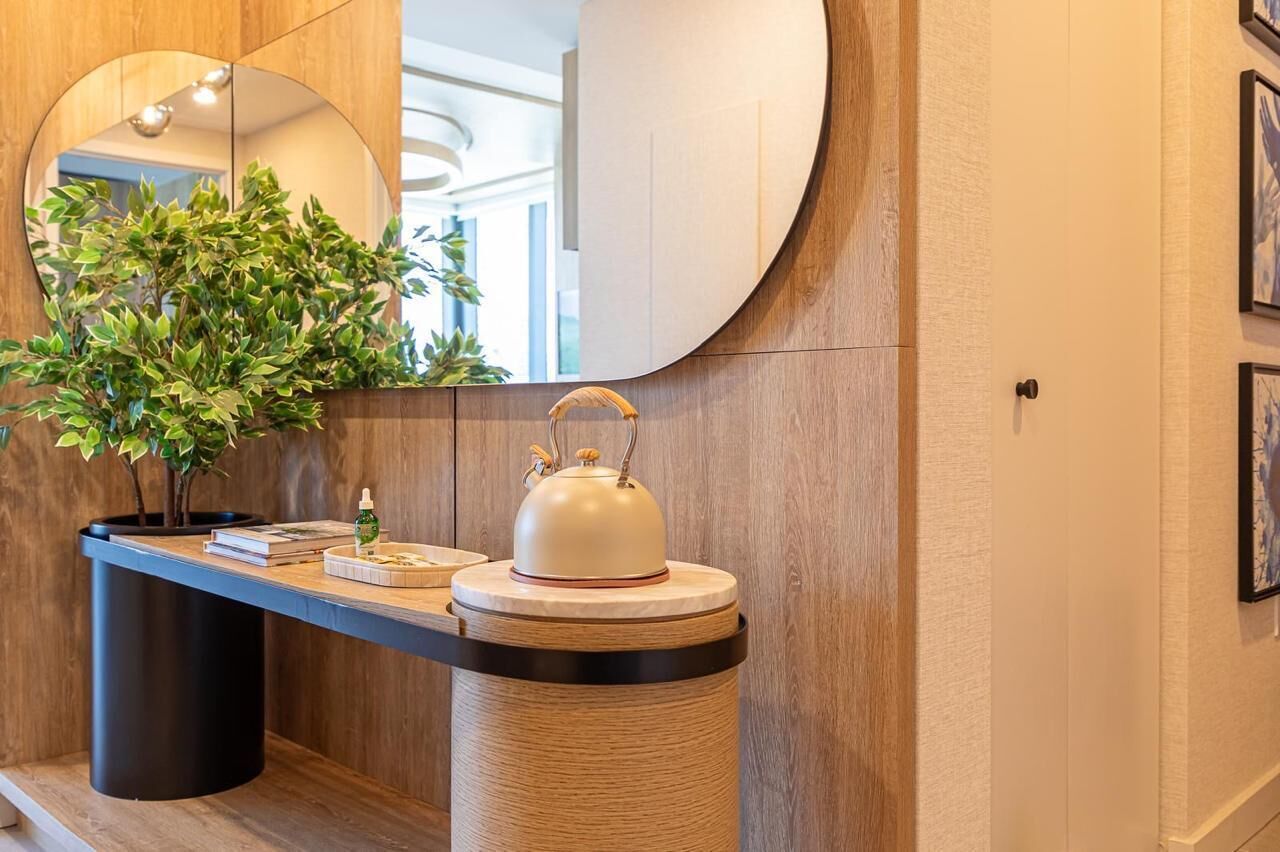 A modern bathroom with a wooden vanity, a round mirror, a potted plant, and a decorative kettle.