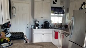 Una cocina con gabinetes blancos, un refrigerador de acero inoxidable, una cafetera y un letrero que dice 'beachhouse'.