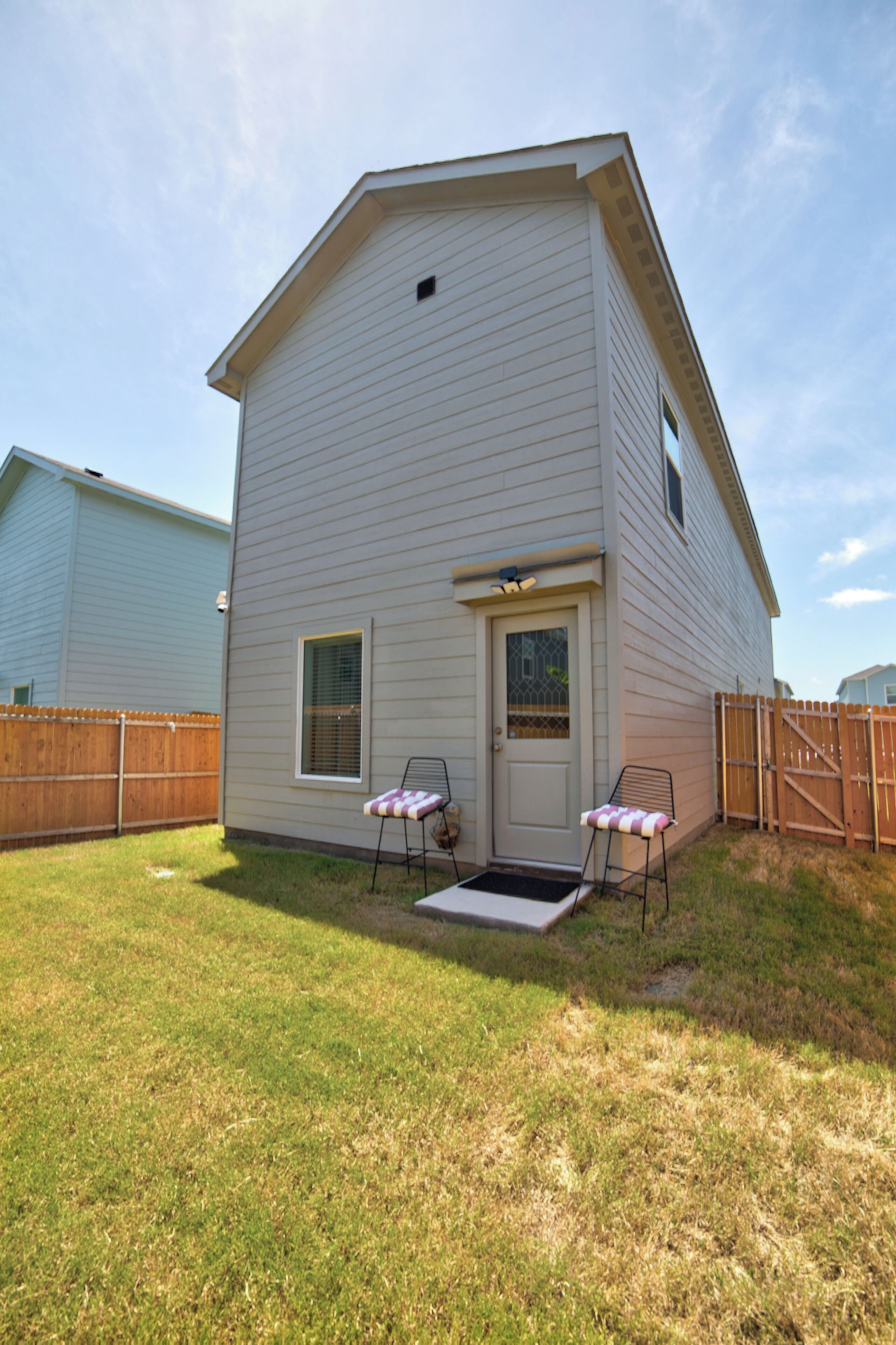 A two-story house with a front door, a small window, and a covered patio area with two chairs.